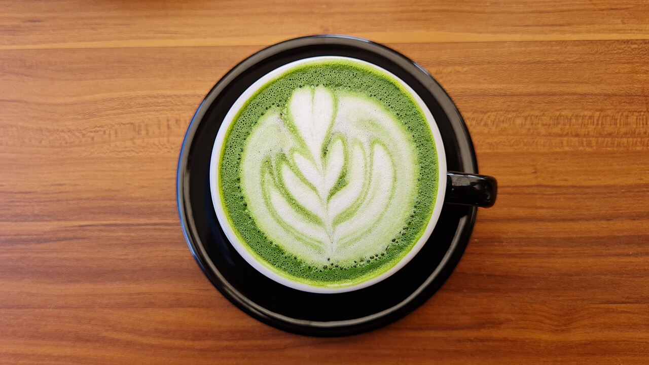 Recette matcha latte en tasse noire avec latte art sur une table en bois